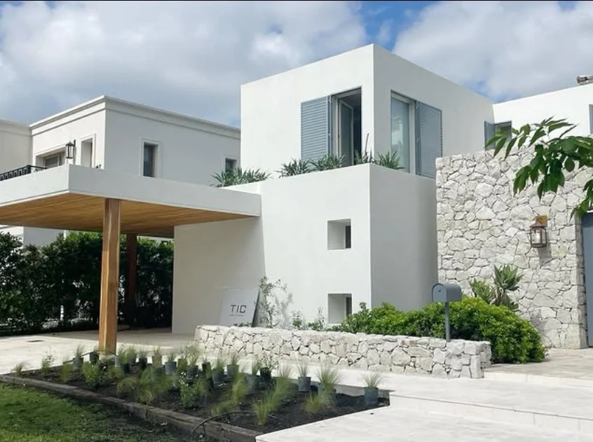 Fachada de Casa Costa con volúmenes blancos, muro de piedra y galería de madera