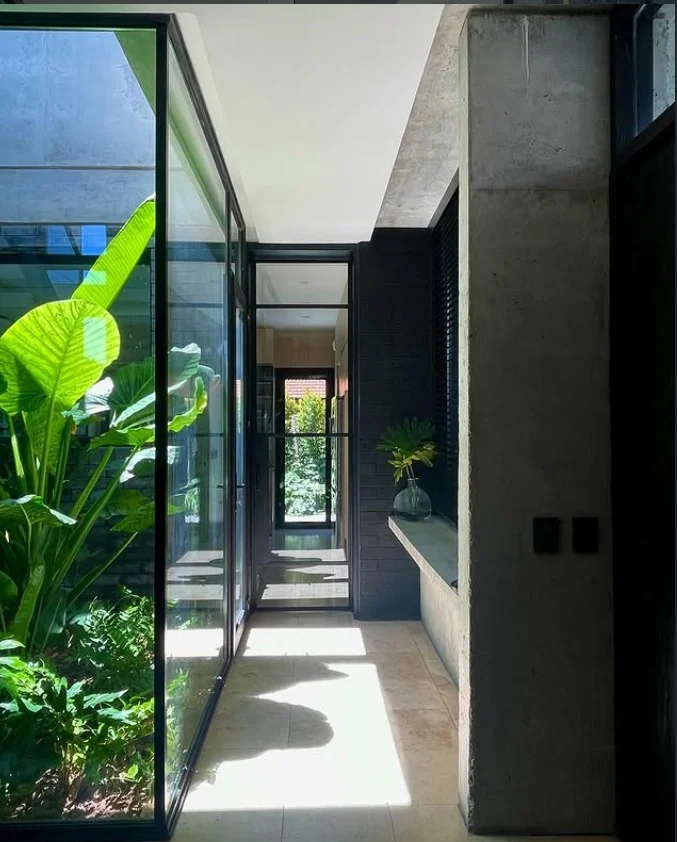 Galería vidriada de Casa Nordelta con patio de plantas y hormigón visto